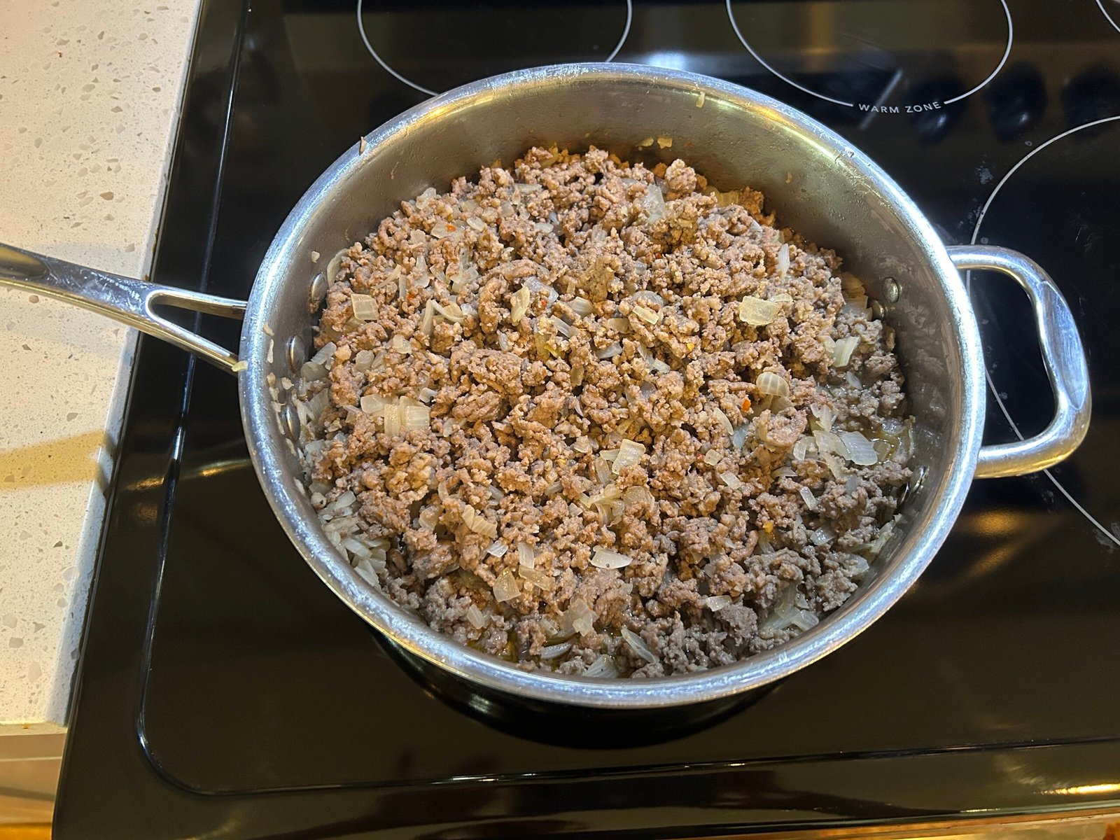 Cooked ground beef, ground sausage , and diced onions in a steel pan in the stove.