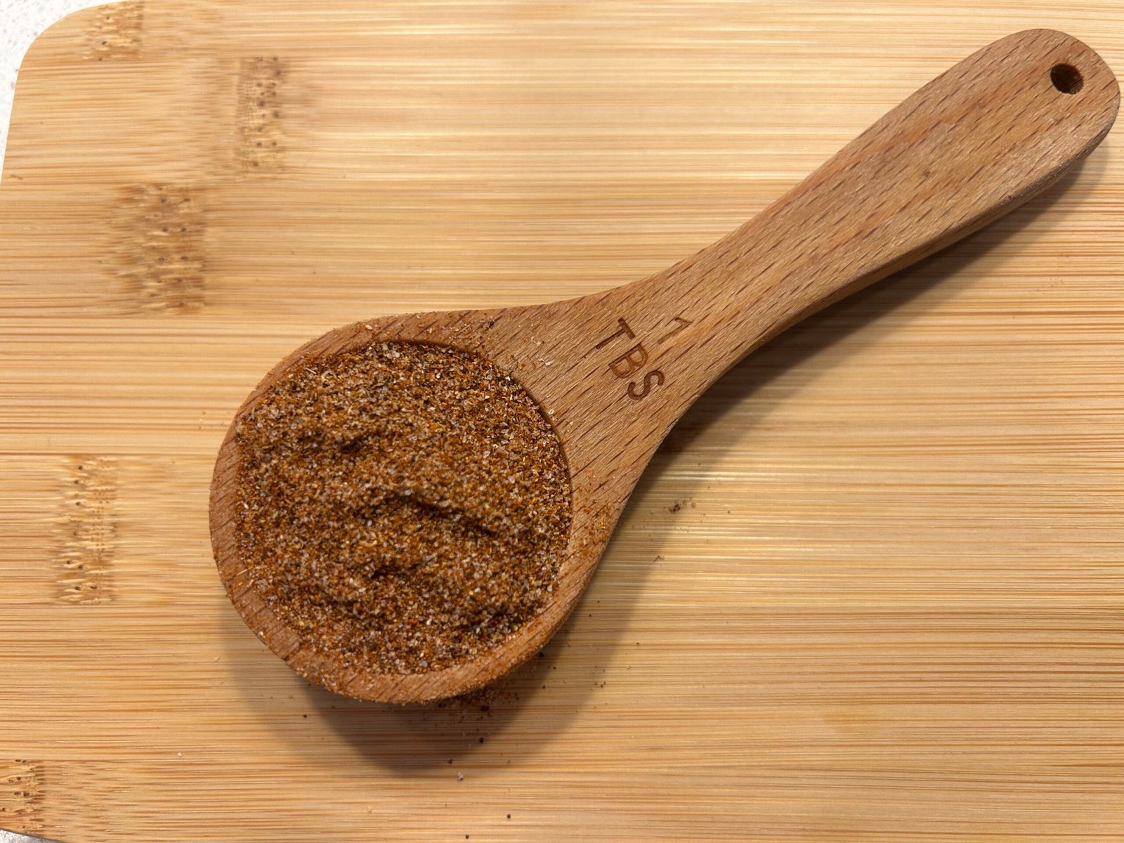 Wooden measuring spoon filled with taco seasoning on a wooden table.