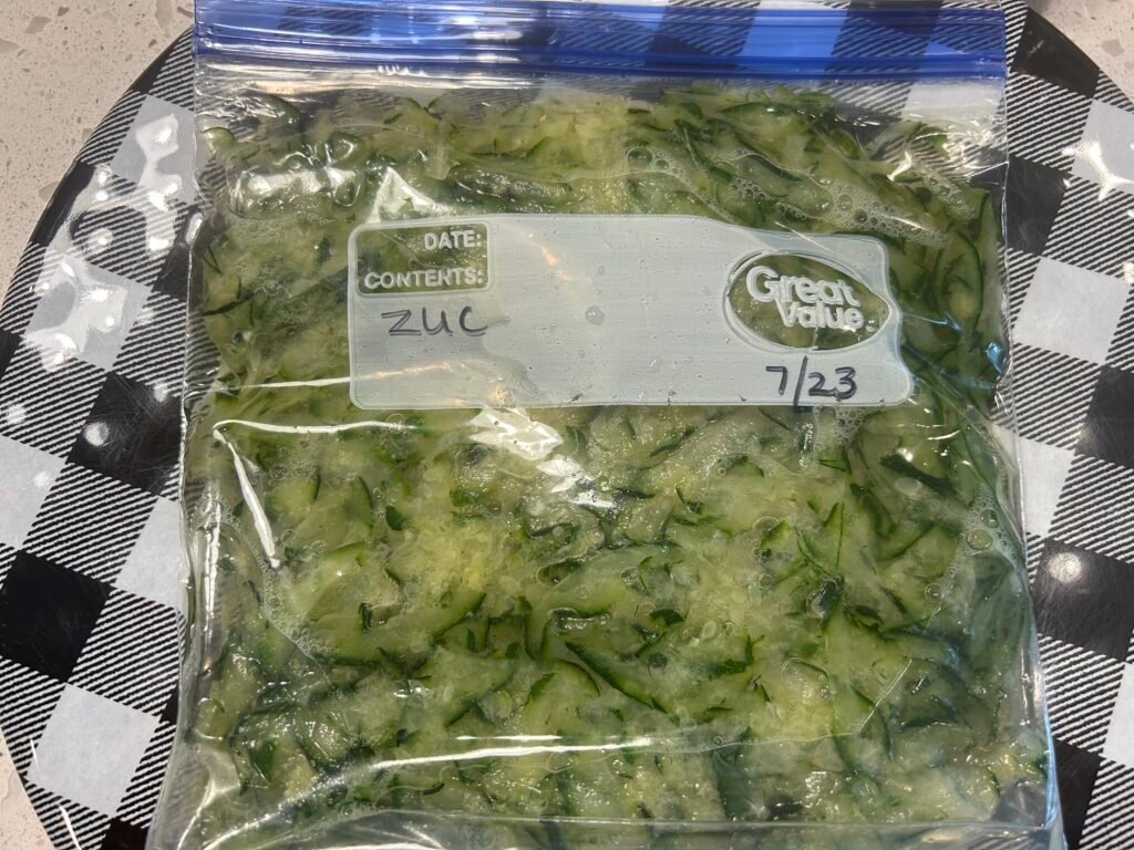 Shredded zucchini in a freezer bag defrosting on a black and white checkered plate.