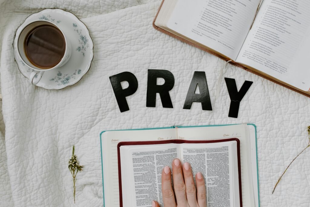 Open bible on a white table cloth under the word pray and a cup of tea