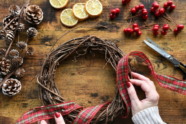 Female creating a holiday Christmas grapevine wreath with plaid ribbon, pine cones, dried lemons