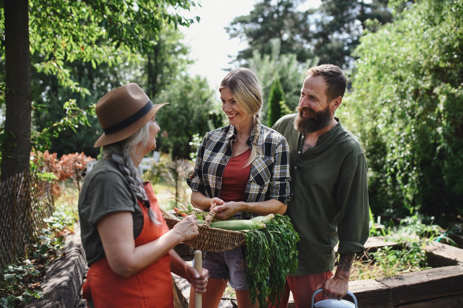 Happy farmers carrying basket with homegrown vegetables outdoors at community farm