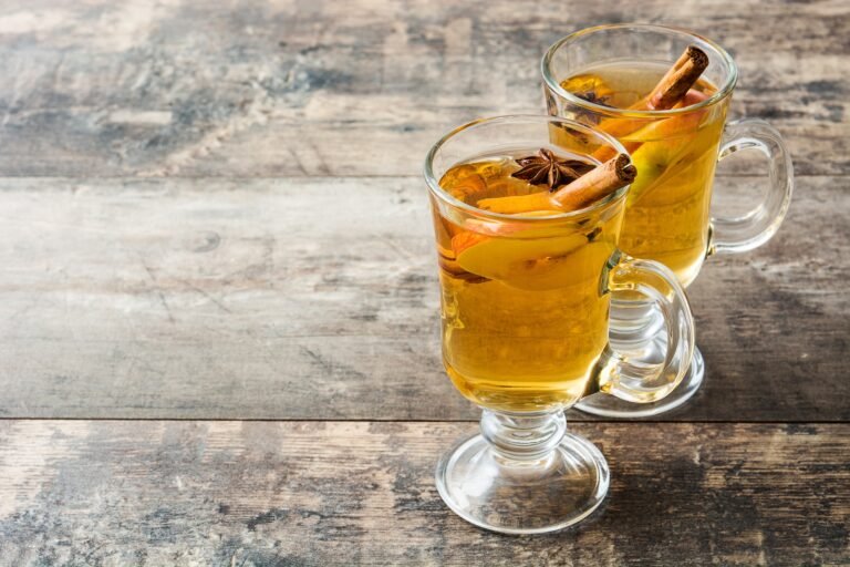 Two glasses of hot apple cider with cinnamon sticks on rustic wooden table